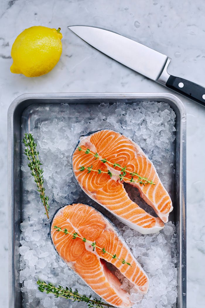 Top view of fresh salmon steaks on ice with lemon, thyme, and knife, showcasing culinary freshness.