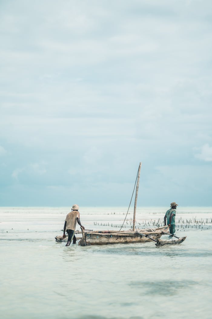 Fishermen navigate a traditional boat along Zanzibar's serene beach, capturing local island culture.